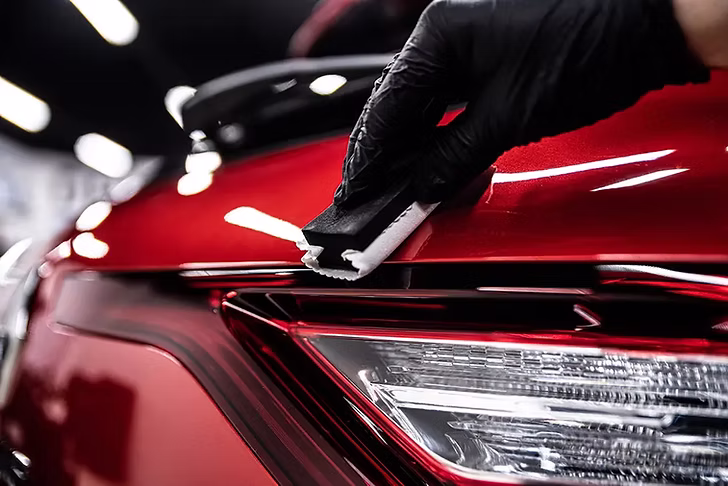 Professional ceramic coating being applied to luxury red vehicle